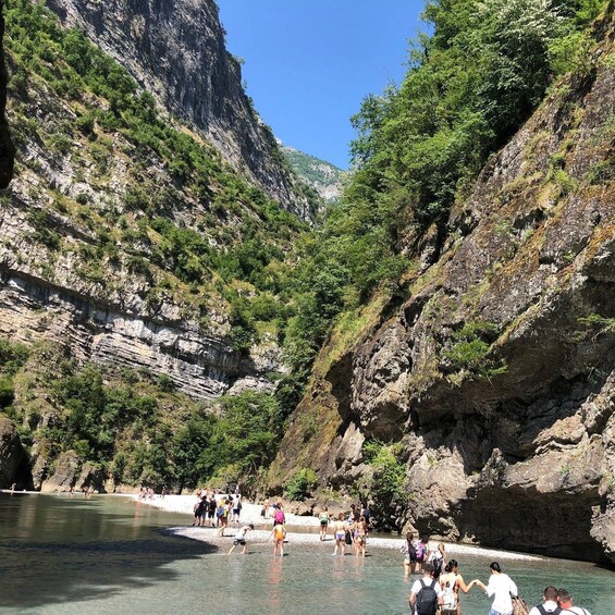 A group of people swimming in a clear, shallow pool surrounded by rocky cliffs and lush greenery. 1