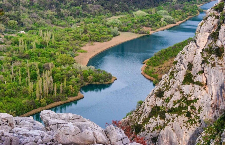 A river winding through a lush valley with rocky cliffs on one side and dense greenery on the other. 2