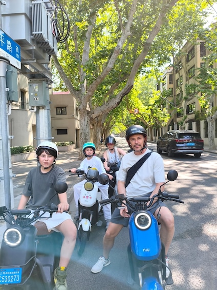 A group of people on scooters on a tree-lined street. 1