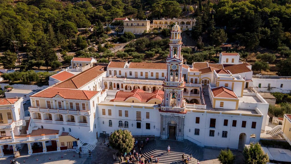 An aerial view of a historic town with white buildings, red-tiled roofs, and a prominent church with a bell tower. 4
