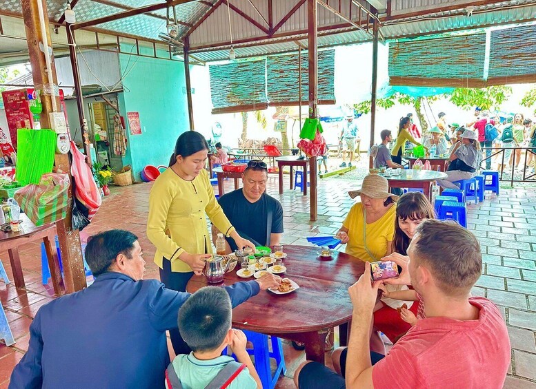 A group of people dining outdoors at a rustic eatery with a tiled floor and wooden tables. 5
