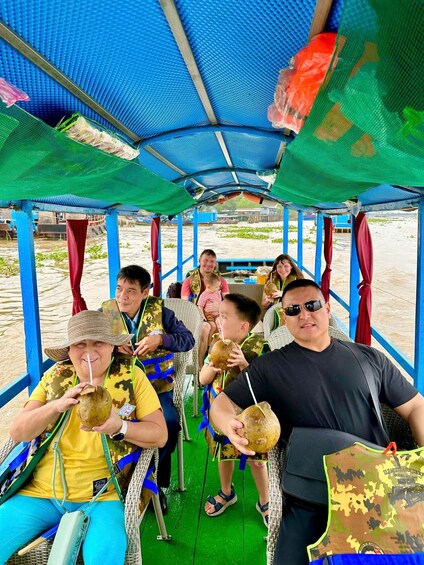 People on a boat with a blue canopy, holding coconuts. 2