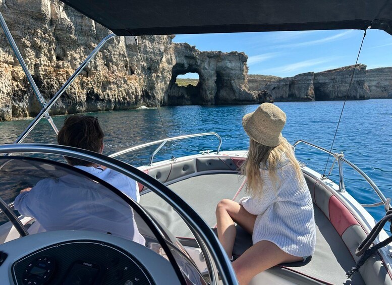 A boat with two people, one wearing a straw hat, and a rocky coastline with a natural arch formation. 1