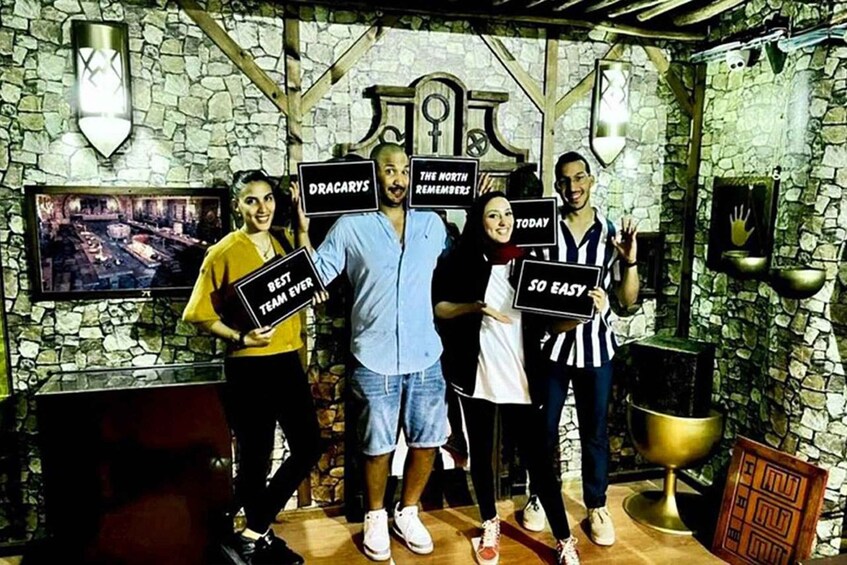 Un gruppo di persone che tiene in mano dei cartelli in una stanza rustica con pareti in pietra e uno schermo televisivo. 5