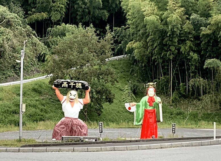 Due persone in abiti tradizionali in piedi lungo una strada, con una foresta sullo sfondo. 4