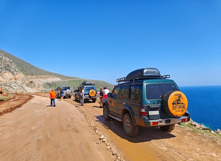 A Jeep Safari vehicle with a luggage rack and a spare tire on a dirt road by the sea. 1