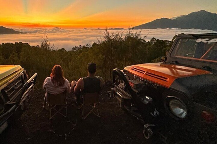 Two people sitting on chairs facing a sunset over a mountainous landscape. 5