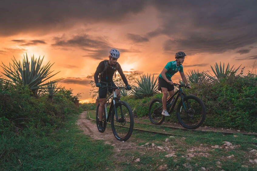 Two cyclists on a dirt path with a sunset in the background. 2