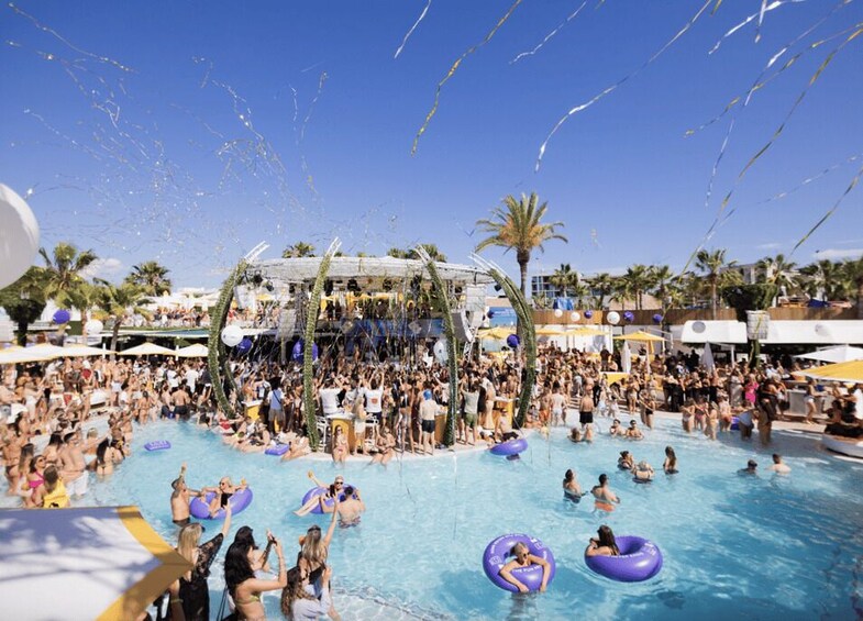 A crowded outdoor swimming pool with people on inflatable rings and a water fountain. 3