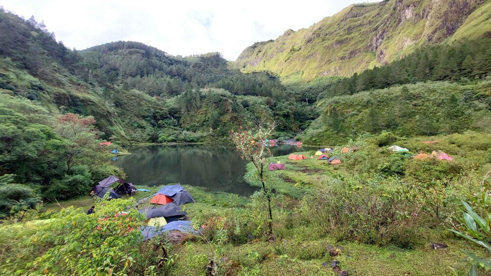A lake surrounded by forested hills with several tents set up on the shore. 5