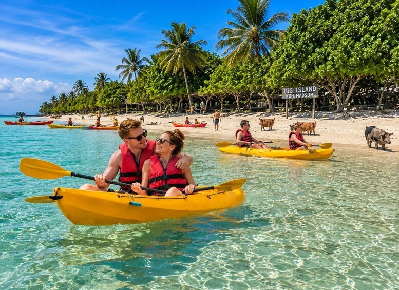 A couple kayaking on clear turquoise water, palm trees, and a beach with a sign reading 'PIG ISLAND KOH MADSUM.' 3