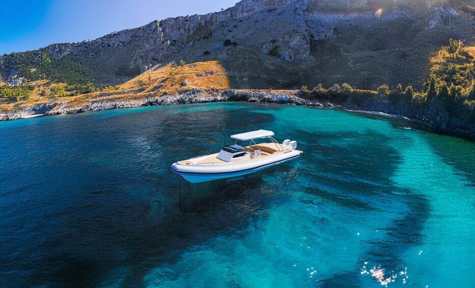 Een kleine boot op helder turquoise water nabij een rotsachtige kustlijn. 5