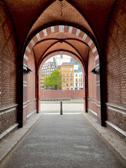 An arched brick tunnel with a view of buildings and a tree in the distance. 2