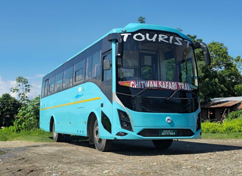 A turquoise bus with 'CHITWAN SAFARI TRAV' written on the side, parked on a dirt road with greenery in the background. 4