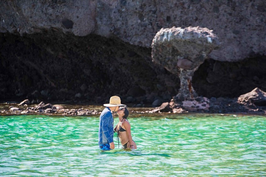 A couple in a clear blue sea with a rocky cliff in the background. 1