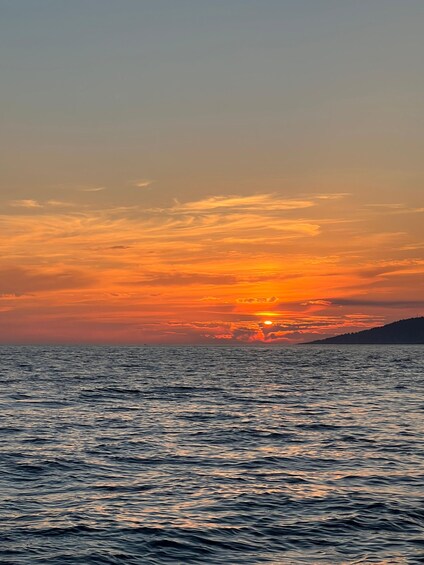 A sunset over the ocean with a silhouette of a hill in the distance. 5