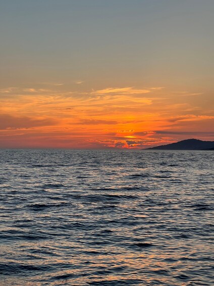 A sunset over a body of water with a silhouette of a landmass in the distance. 2