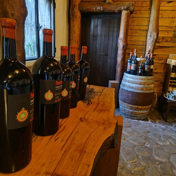 Bottles of Proclamation wine on a wooden table in a rustic setting with a wooden barrel and a stone floor. 3