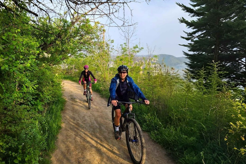Three cyclists on a dirt path surrounded by greenery and trees. 5