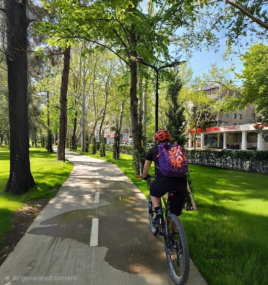 A cyclist on a paved path surrounded by trees and grass. 3