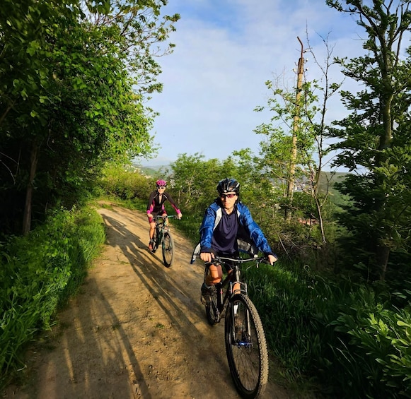 Two cyclists on a dirt path surrounded by greenery. 4