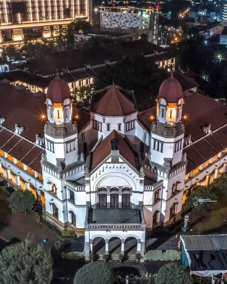 A large, historic building with two prominent towers and a central dome, surrounded by other buildings and trees. 2