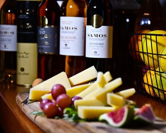 A selection of wine bottles, cheese, grapes, and citrus fruits on a wooden board. 3