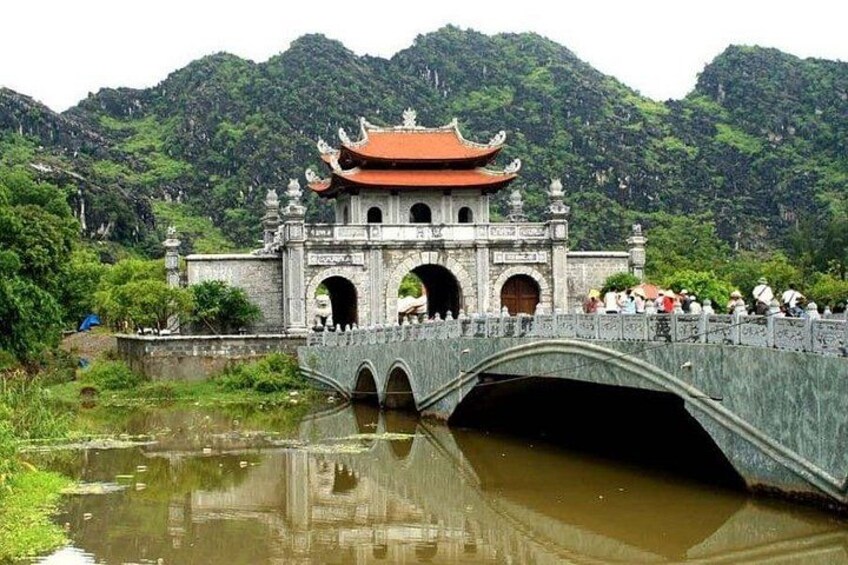 A traditional Chinese-style bridge with a red roof, leading to a gate with arches, surrounded by lush greenery and hills. 2