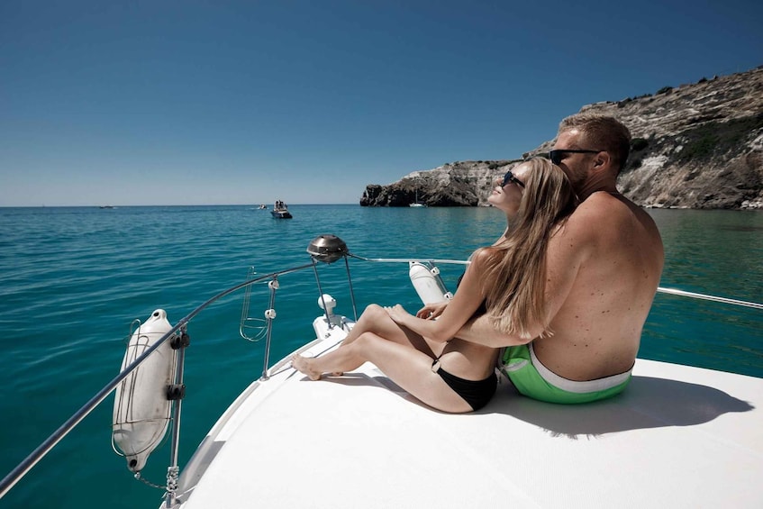 A couple on a boat in clear waters with a rocky coastline in the background. 1