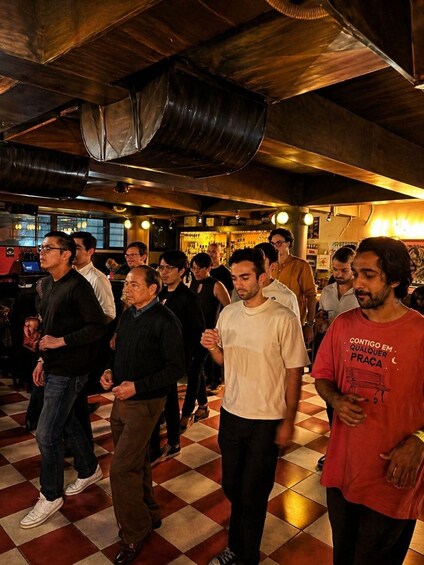 A group of people in a dimly lit bar with checkered flooring and exposed ductwork. 2