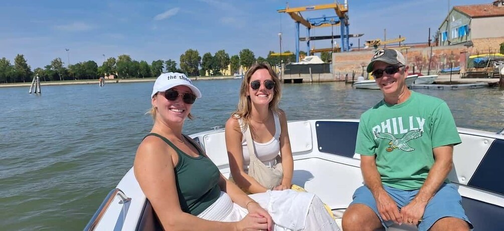 Three people on a boat with a water body and industrial structures in the background. 1