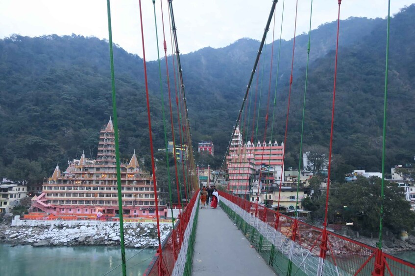 A suspension bridge with red and green cables, leading to a temple complex with multiple buildings. 2
