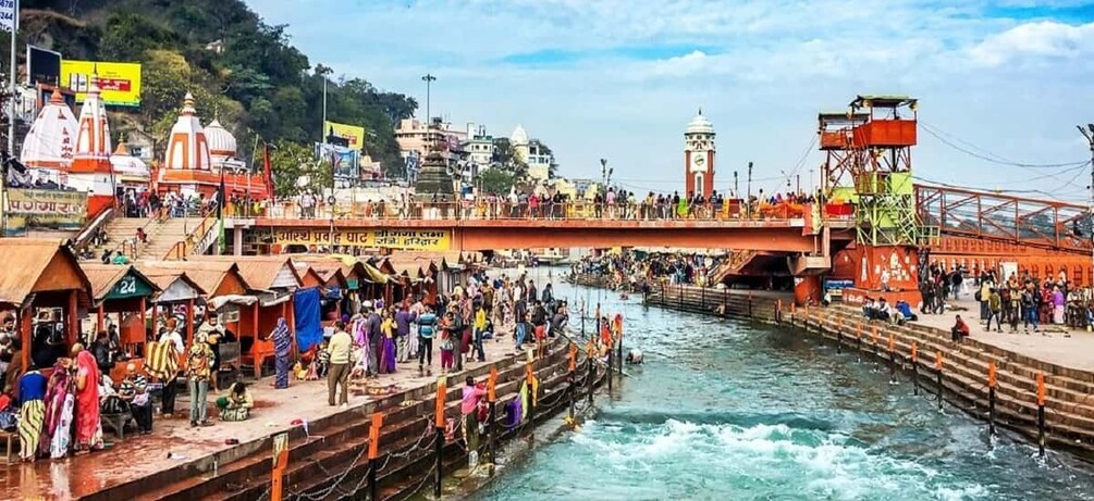 A crowded riverside with a bridge, boats, and people. 4