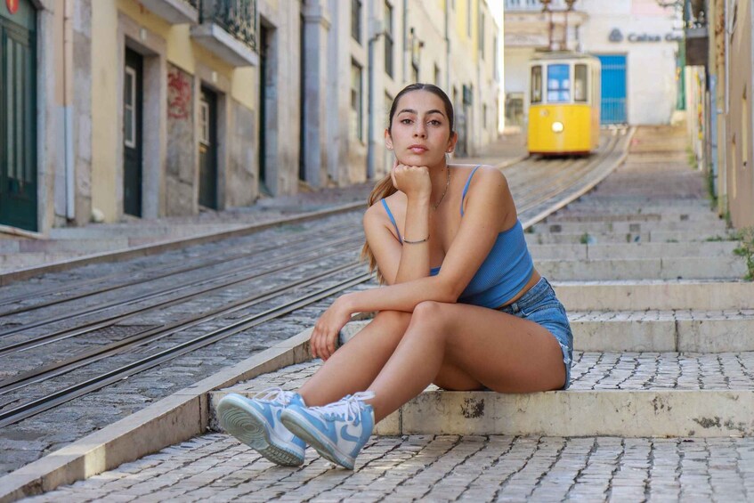 A person sitting on steps by a train track in an urban setting with buildings and a tram in the background. 1