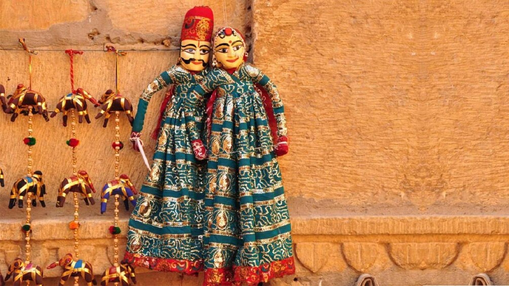 Two figures in traditional attire with intricate patterns, standing against a textured wall. 4