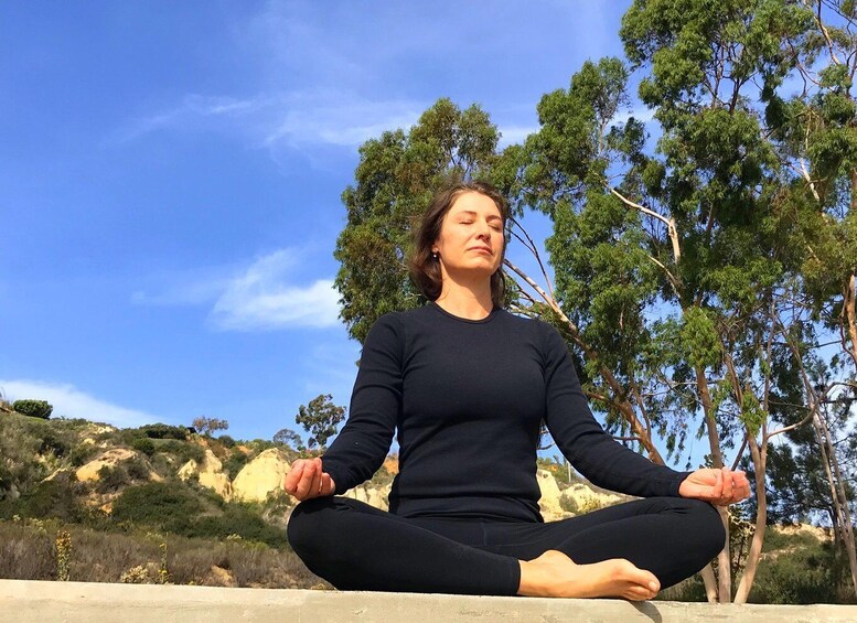 A person meditating in a natural outdoor setting with trees and hills in the background. 2