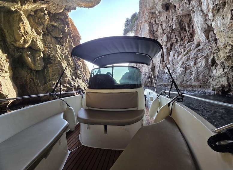 A boat's interior with a canopy, wooden deck, and rocky cliffs in the background. 3