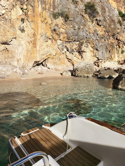 A boat's deck with clear water and rocky cliffs in the background. 2