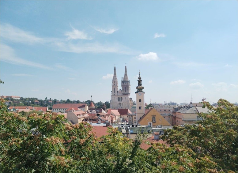 A cityscape with a prominent church tower and a smaller adjacent tower, surrounded by residential buildings and greenery. 3