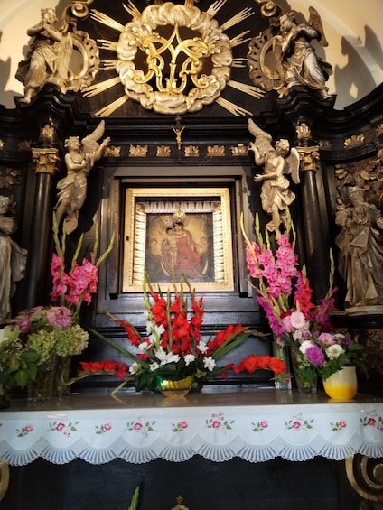 A religious shrine with ornate carvings, a framed religious painting, and floral arrangements. 4