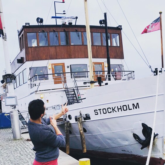 Henkilö osoittaa sormellaan laivaan, jonka nimi on STOCKHOLM ja joka on ankkuroitu laituriin. 4