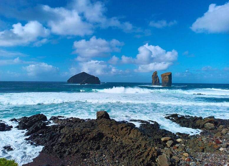 A rocky coastline with waves crashing against the rocks and two prominent rock formations in the distance. 5