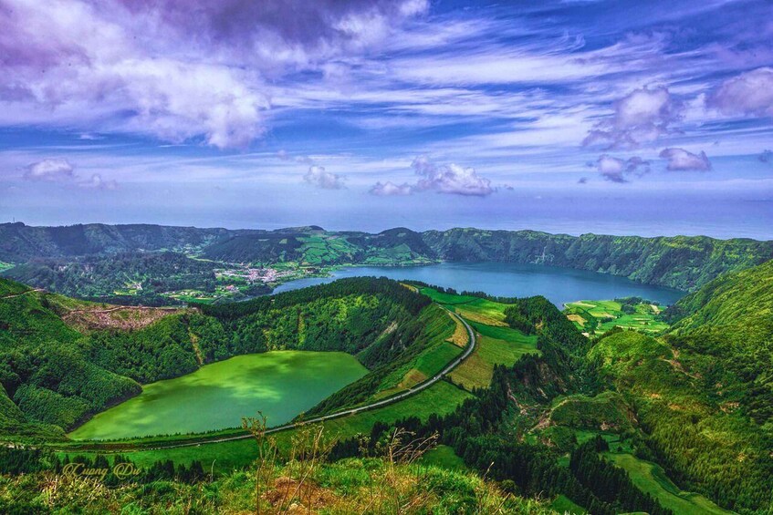 A lush green valley with a lake, a winding road, and a distant town. 1