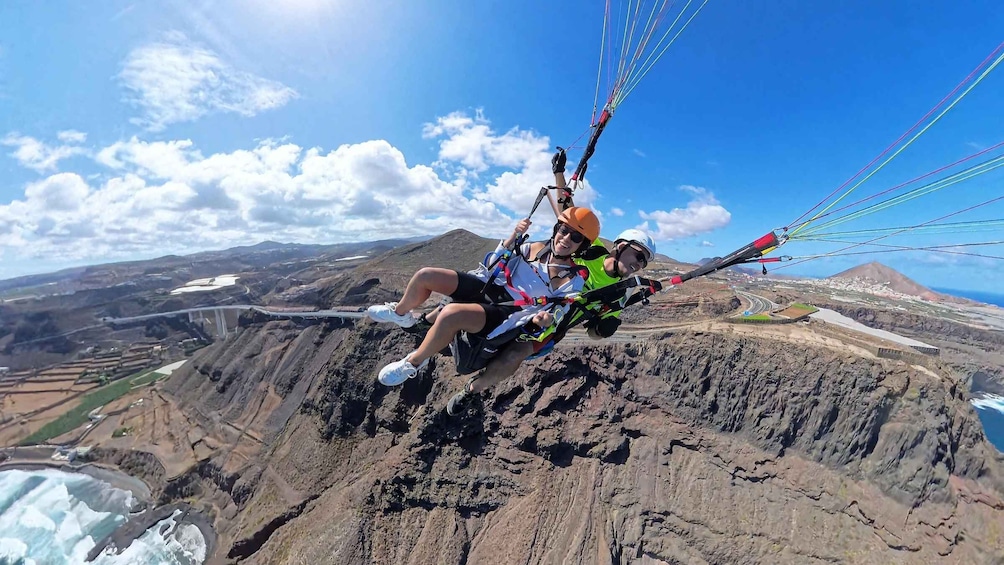 A person paragliding over a rugged landscape with mountains and a coastal area in the background. 4