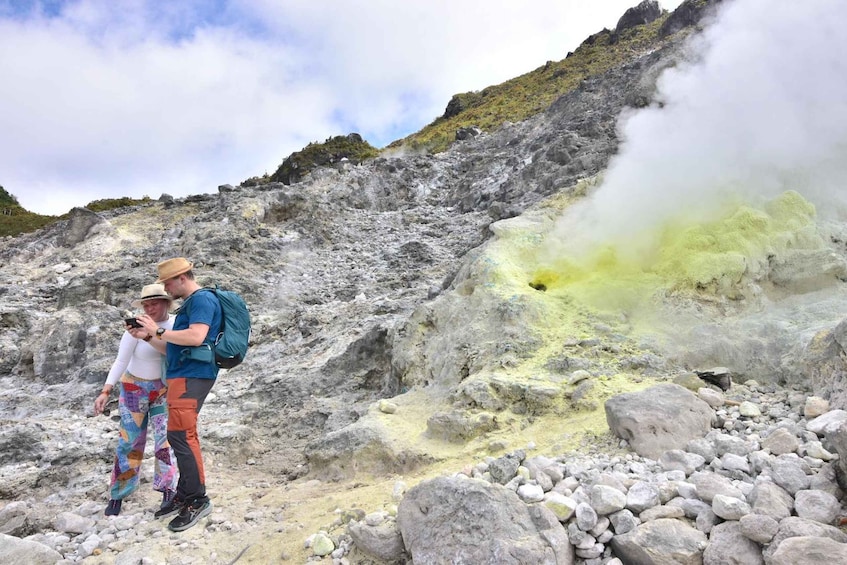 A volcanic landscape with a person and a child observing a geothermal area with yellow and white steam. 5