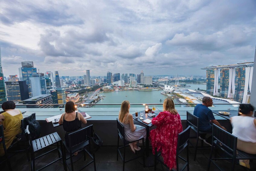 A group of people dining at a table with a view of a city skyline and a river. 1