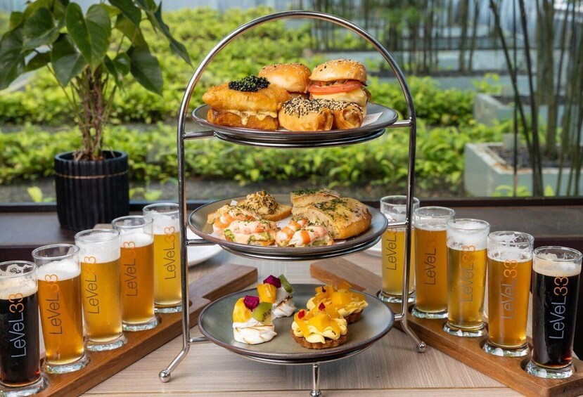 A tiered serving tray with various food items and glasses of beer. 4