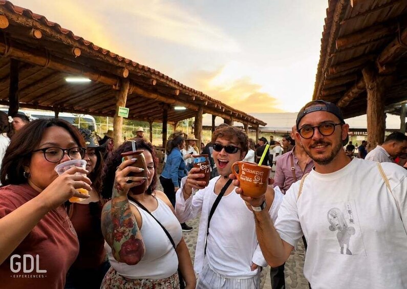 A group of people at an outdoor event with a covered area and a sunset in the background. 2