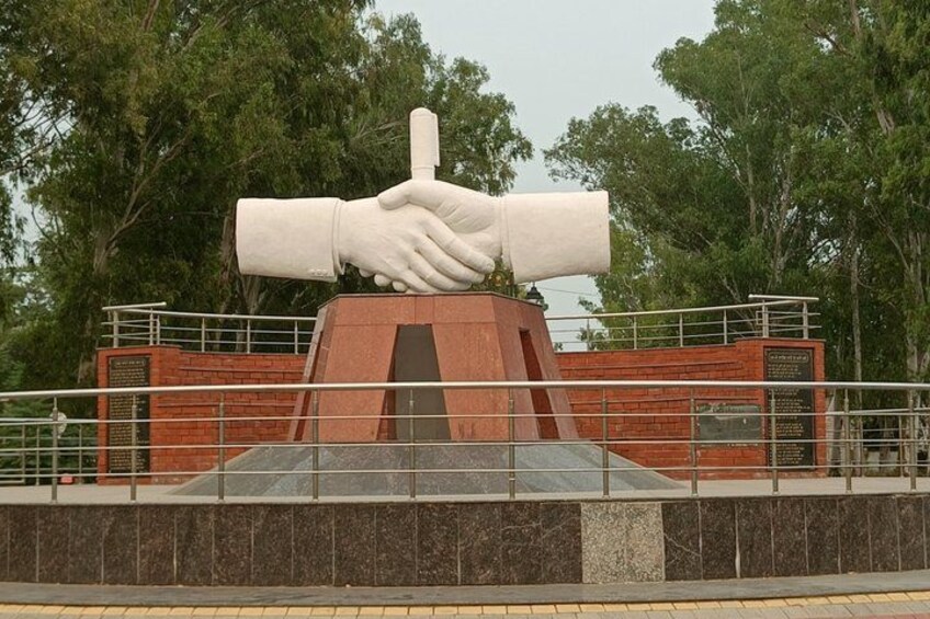A large sculpture of two hands shaking, surrounded by a brick structure and a stone base, with trees in the background. 5
