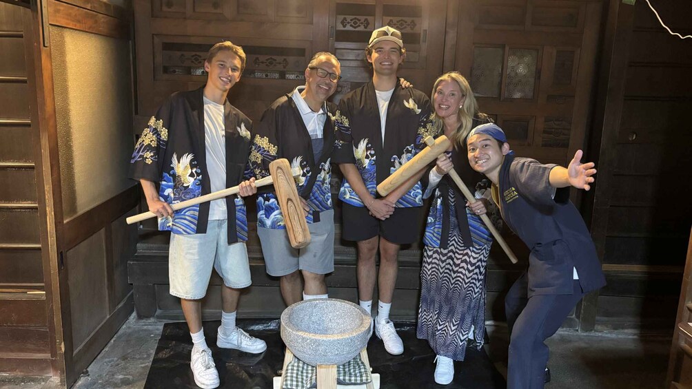 A group of people in traditional attire holding wooden tools, standing in a wooden room with decorative panels. 3